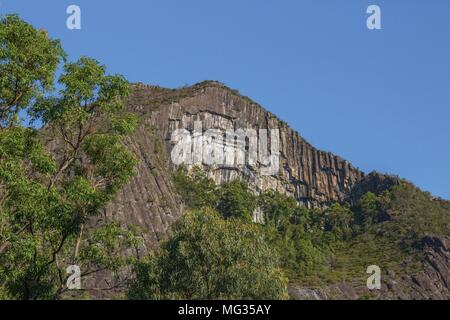 Jutts falaise vertigineuse au-dessus de la limite des arbres d'une clairière au pied de la montagne. Soutenue par un ciel bleu clair. Banque D'Images