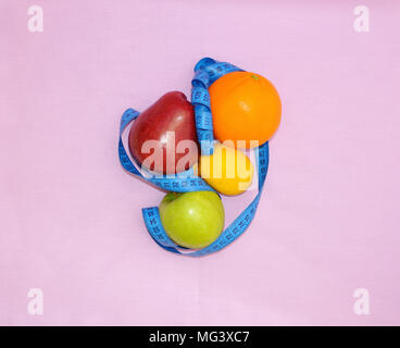 Les pommes, citron et orange enveloppée avec un mètre de tailleur bleu sur fond rose, vue du dessus Banque D'Images