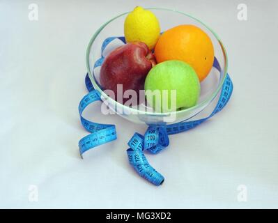 Des fruits sains dans un bol en verre, entourée d'un mètre de tailleur bleu, fond bleu, top side view Banque D'Images
