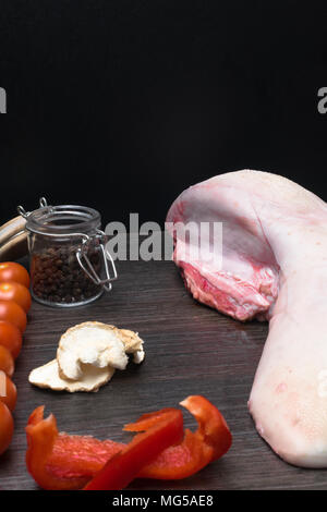 La langue de porc ou de boeuf aux légumes - le céleri, le poivre noir et rouge, l'ail, l'oignon, se trouve sur une planche à découper, sur fond noir, close-up Banque D'Images