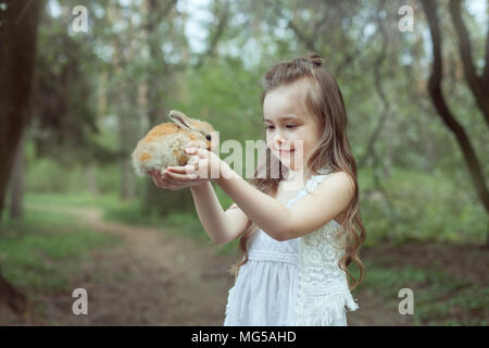 Petite fille se dans les bois et est titulaire d'un petit lapin dans ses mains. Banque D'Images