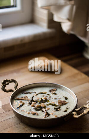 Yuvalama turc avec soupe de yaourt et de pois chiches dans un bol de cuivre sur une surface en bois. Banque D'Images