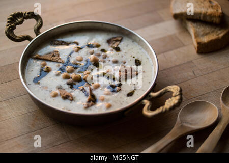 Yuvalama turc avec soupe de yaourt et de pois chiches dans un bol de cuivre sur une surface en bois. Banque D'Images