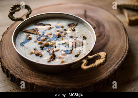 Yuvalama turc avec soupe de yaourt et de pois chiches dans un bol de cuivre sur une surface en bois. Banque D'Images