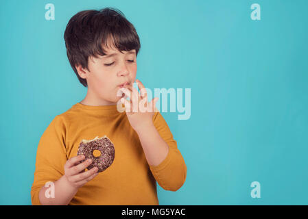 Boy eating donut sur fond bleu Banque D'Images