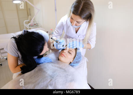 Cosmetologist professionnel faire le maquillage permanent pour la femme au sein du cabinet avec l'infirmière. Banque D'Images