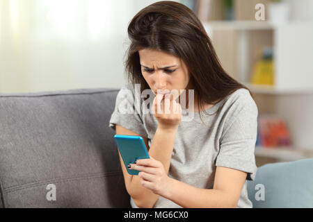 Girl biting nails nerveux contenu téléphone lecture assis sur un canapé dans la salle de séjour à la maison Banque D'Images