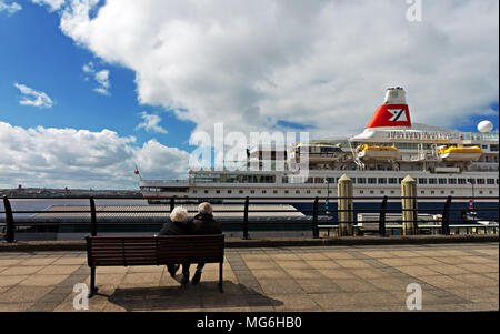 Un couple de personnes âgées assis sur un banc, regarder les 'Black Watch' un navire de croisière Fred Olson comme il prend les passagers à Liverpool UK. Banque D'Images