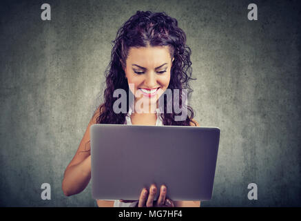 Casual young blonde shopping online using laptop and smiling heureusement sur gris grunge mur. Banque D'Images