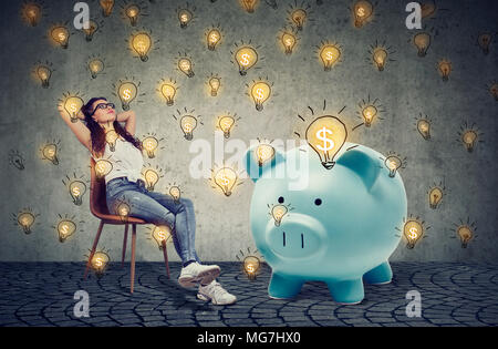 Young casual businesswoman with big tirelire relaxing sitting on chair générer idées bsuiness Banque D'Images