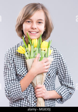 Belle fille avec bouquet de fleurs sur fond gris. Enfant souriant avec bouquet de tulipes jaunes comme un cadeau. Heureux les mères, anniversaire ou Saint Valentin Banque D'Images