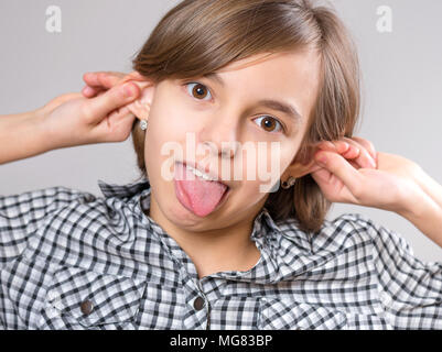 Silly girl des grimaces - funny monkey face. Enfant avec de grandes oreilles, sur fond gris. Portrait d'émotionnel caucasian teenager looking at camera. Banque D'Images