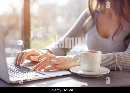 Une fille travaille derrière un ordinateur portable dans un café, les doigts en tapant sur le clavier. Lieu de travail dans un café, une tasse de café à côté d'un ordinateur portable, lumineuse, ensoleillée phot Banque D'Images