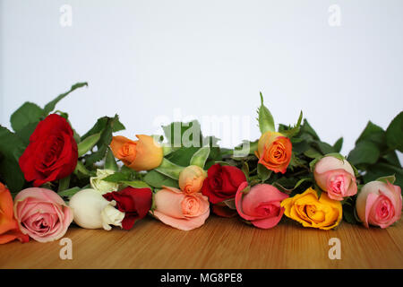 Bouquet de fleurs roses de beaucoup de couleurs posées sur une table en bois clair et sur un fond blanc Banque D'Images