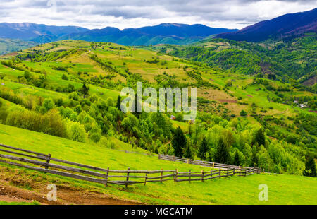 Clôture en bois le long de la colline herbeuse. beau printemps paysage de montagnes des Carpates un jour nuageux. Banque D'Images