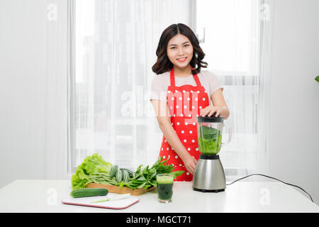 Young smiling woman making avec smoothie vert frais dans le bol mélangeur dans la cuisine à la maison. Smoothie végétarien sain pour la perte de poids et de désintoxication Banque D'Images