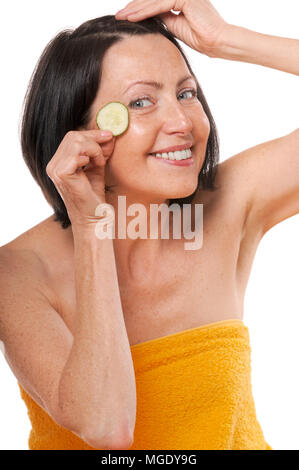 Cheerful mature woman holding morceau de concombre près de ses yeux. Traitement spa naturel. Isolé sur fond blanc Banque D'Images