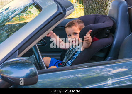 Rire heureux enfant dans un siège convertible dans la voiture un siège pour enfant et montre les pouces vers le haut. Banque D'Images