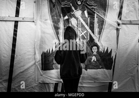 Un pauvre enfant réfugié prie devant un tissu représentant un imam orthodoxe dans le camp de réfugiés de Calais, Jungle, en Europe Banque D'Images