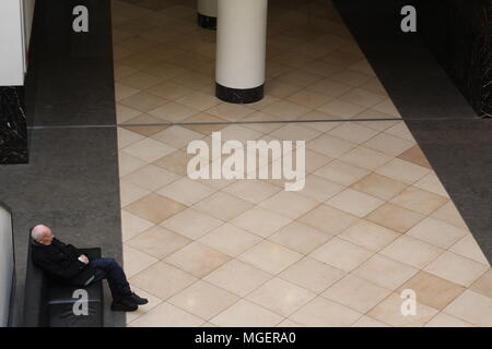 Monsieur âgé attend assis sur une chaise à l'angle du cadre de la création d'un jeu de symétrie avec le sol et les colonnes Banque D'Images