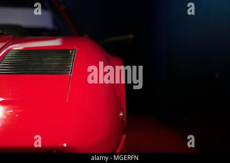 Museau rouge d'une Ferrari Testarossa qui dépasse du mur, avec le logo Ferrari bien éclairé et le reflet de la lumière sur le capot Banque D'Images