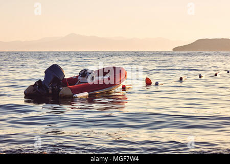 Gonflable rouge sanglier moteur sur une mer calme au coucher du soleil Banque D'Images