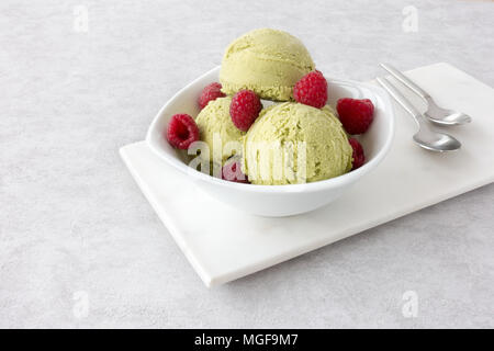 Bol rempli de boules de crème glacée maison vert matcha et framboises fraîches sur une planche à découper en marbre blanc. Banque D'Images