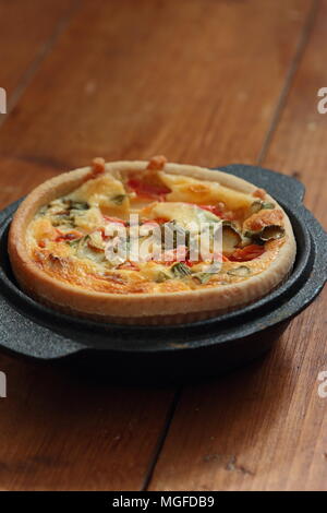 Quiche aux tomates et oignons dans un plat en fonte sur un fond de bois Banque D'Images