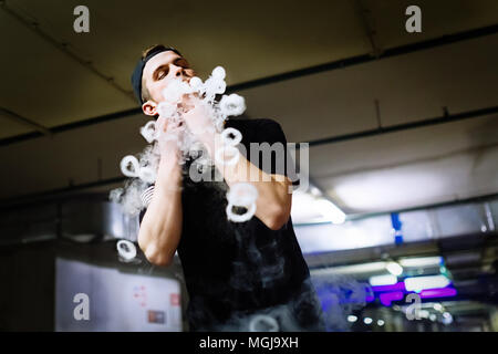 L'homme à la fumée secondaire d'une cigarette électronique et libère des vapeurs de nuages d'effectuer divers genre d'vaping astuces Banque D'Images