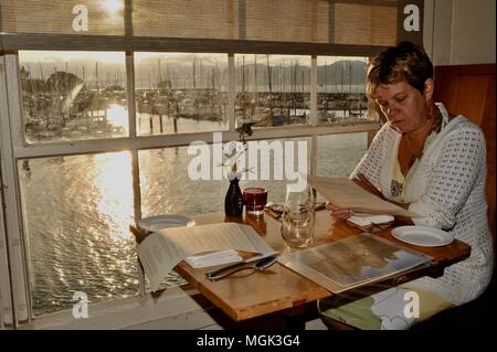 Femme d'âge moyen du menu Lecture, coucher du soleil à lumineux verts Restaurant (végétarien), Fort Mason Center, Marina District, à San Francisco, Californie, USA. Banque D'Images