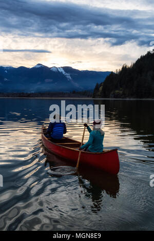 Les gens aventureux sur un canot en bois sont profiter du beau paysage de montagne canadiens lors d'un coucher du soleil vibrant. Pris dans la rivière Harrison, à l'Est de Banque D'Images