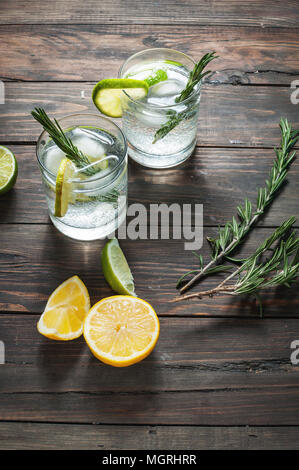 Verre à cocktail gin tonic avec du citron, du romarin et de la glace sur une table en bois rustique Banque D'Images