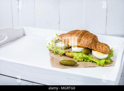 Sandwich croissant au thon, oeuf dur, salade et concombre sur bac blanc le petit-déjeuner gratuit. Copy space Banque D'Images