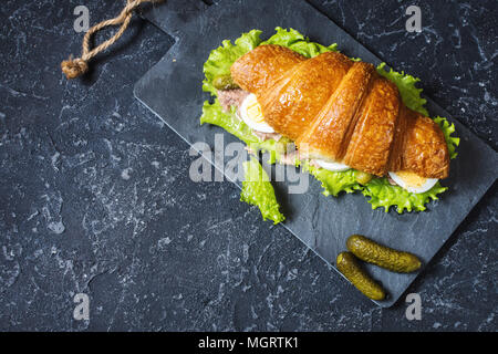 Sandwich croissant au thon, oeuf dur, salade et concombre sur table en pierre. Copy space Banque D'Images