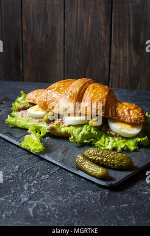 Sandwich croissant au thon, oeuf dur, salade et concombre sur table en pierre. Banque D'Images