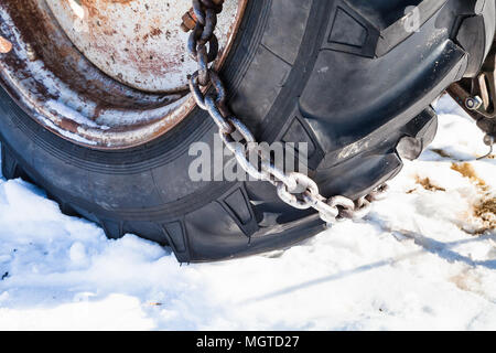 Chaîne neige monté sur le pneu du tracteur sur la route couverte de neige close up Banque D'Images