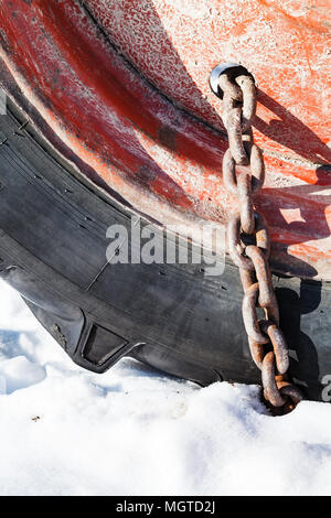 Chaîne à neige rouillée monté sur la roue du tracteur sur la route couverte de neige close up Banque D'Images