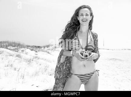 Ambiance bohème locations. Style gitan Portrait of smiling young woman in bikini sur la plage avec retro photo caméra Banque D'Images