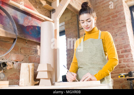 Taille portrait of pretty young woman wearing apron travail du bois dans l'élaboration d'Shop, debout contre le mur de briques, copy space Banque D'Images
