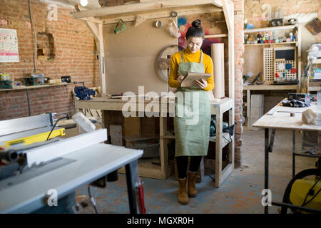 Portrait de jeune femme moderne portant un tablier écrit dans l'ordinateur portable tout en travaillant dans des lofts boutique artisanat, copy space Banque D'Images