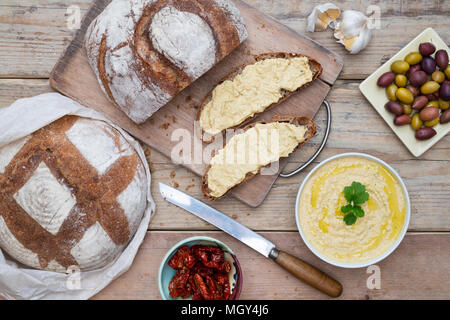 Pain au levain et pain au levain d'épeautre avec du hoummos, olives et tomates séchées sur une carte de pain. UK Banque D'Images