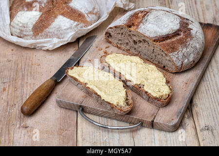 Pain au levain et pain au levain d'épeautre avec du hoummos sur une carte de pain. UK Banque D'Images