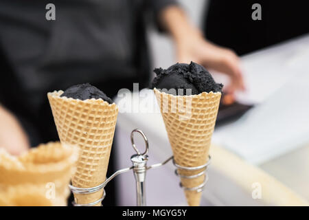 Close-up de deux cônes alvéolés, les cornes avec des boules de glace noire à la mode et de la main du vendeur. Partie de refroidissement pour le plaisir délicieux. Focus sélectif. R Banque D'Images