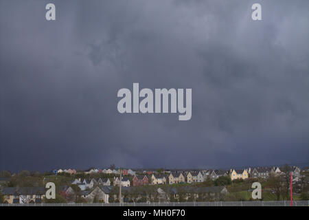 Les nuages de tempête sombre réunissant plus de la maisons peintes de couleurs vives sur la crête au-dessus d'une petite ville dans le comté de Cork, Irlande. Banque D'Images