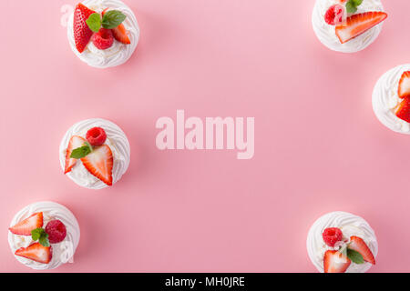 À partir de au-dessus de peu servi avec les baies fraîches desserts meringue sur le dessus sur la surface rose. Banque D'Images