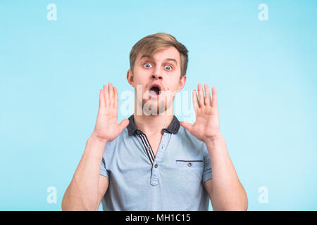 Closeup portrait of étourdis surpris jeune homme les yeux et la bouche grande ouverte, les mains dans l'air de crier crier crier sur fond bleu. L'expression faciale des émotions négatives sentiment Banque D'Images