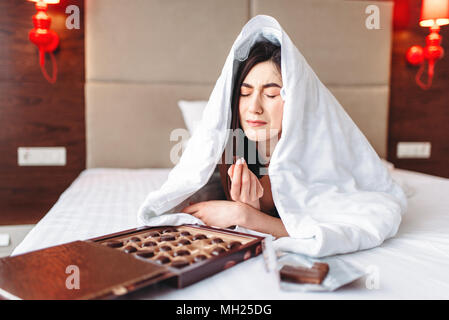 Femme se trouve sous la couverture et mange des bonbons Banque D'Images