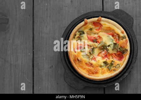 Quiche aux tomates et oignons dans un plat en fonte sur un arrière-plan couleur sélective avec bois Banque D'Images