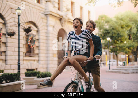 Couple sur un vélo dans la ville. Cheerful woman sitting sur guidon de vélo de petits amis. Banque D'Images