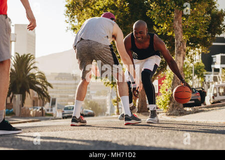 Les hommes jouant au basket-ball jeu sur une journée ensoleillée sur une rue vide. Les hommes pratiquant le basket-ball ses dribbles sur rue. Banque D'Images